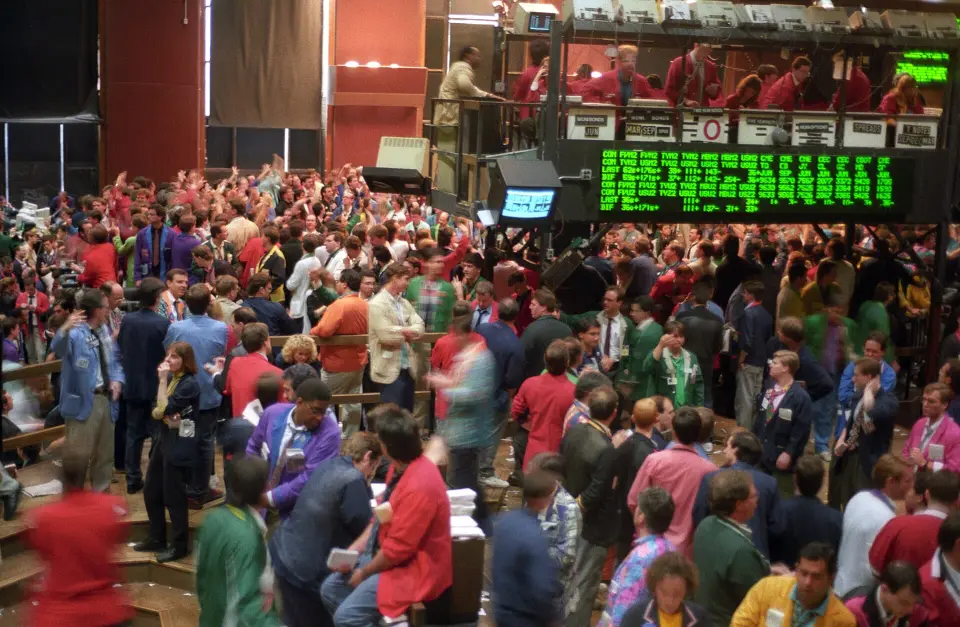 A crowded futures trading floor with traders in coloured jackets under a price board